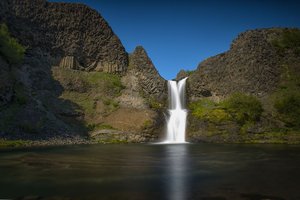 A stunning view of the Selfoss Waterfall cascading into a river, surrounded by natural beauty and rugged terrain