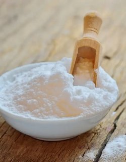 A bowl of baking soda with a wooden spoon resting on top, ready for use in baking or cooking